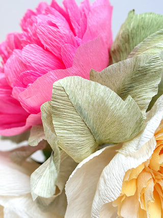 Close up of handmade paper leaves and peonies. the texture and fold of the paper create a realistic feel to the arrangement