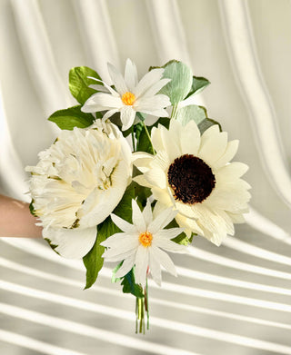 A handcrafted paper bouquet featuring a pale yellow sunflower, white daisy poms, and a hand-painted blush garden peony nestled among lemon leaf and silver dollar eucalyptus, each bloom meticulously shaped for lifelike texture and gathered into an elegant arrangement of soothing neutral tones.