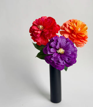 Colorful red, orange and purple paper zinnia flowers in a black vase on a light gray background