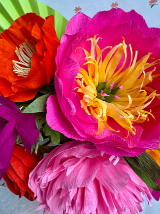 Colorful paper flowers in pink, orange, and purple with a yellow center on a light blue background.