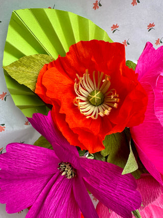 Colorful paper flowers with a green cardstock palm on a patterned background